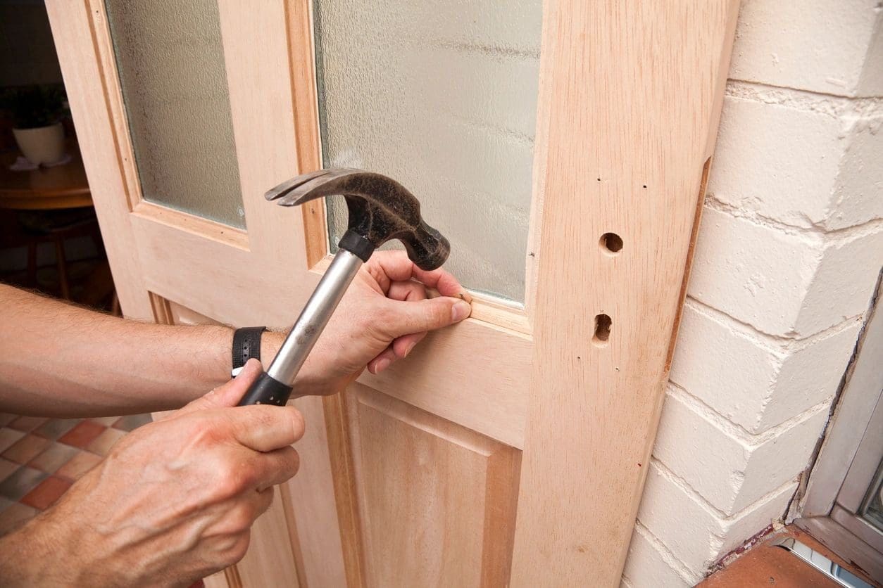 A person holding hammer and nails in front of door.