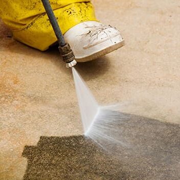 A person using a high pressure washer on the floor.