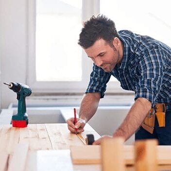 A man working on a table with a drill and some wood.