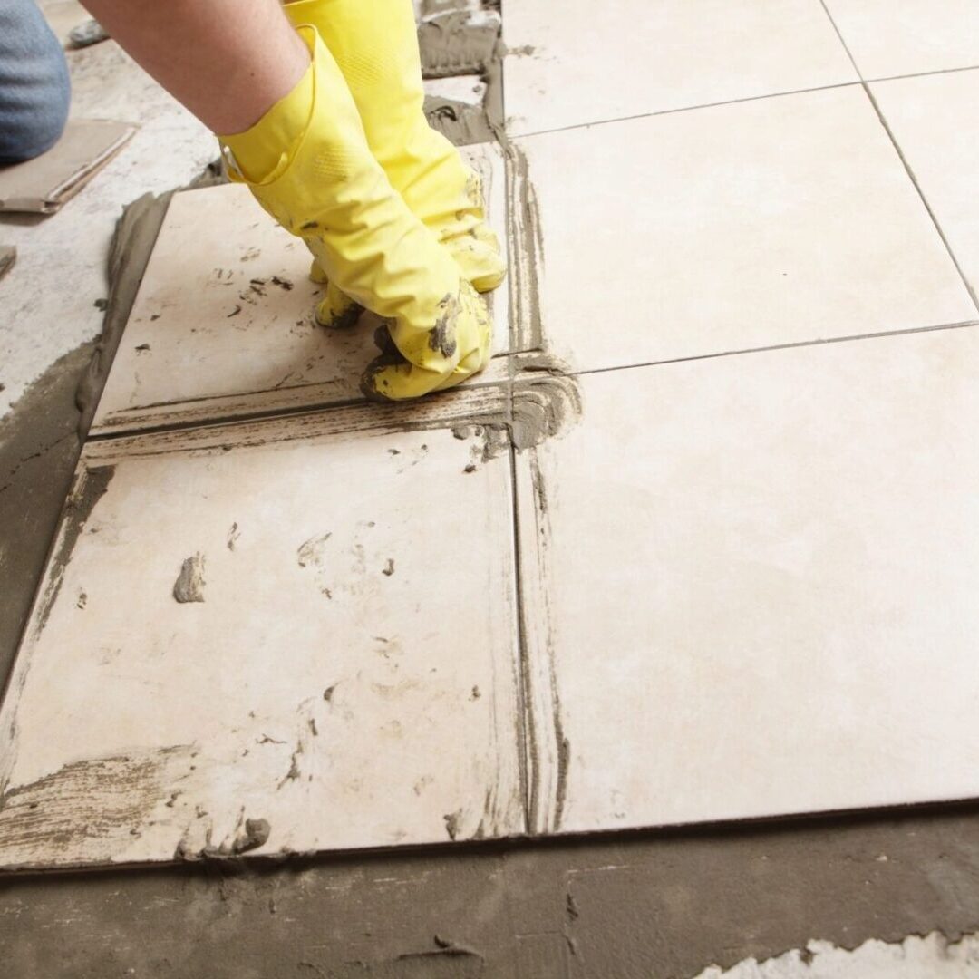 A person in yellow gloves is laying tile on the floor.