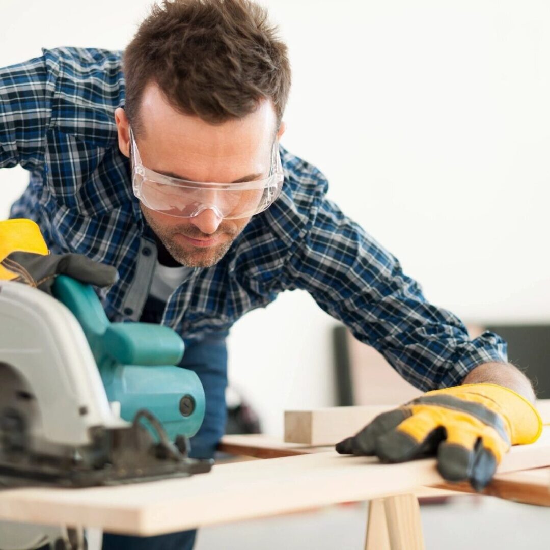 A man wearing safety glasses and gloves using a circular saw.